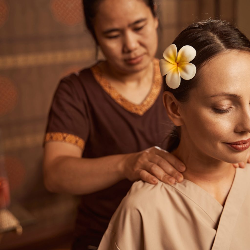 Serene young woman sitting with her eyes closed during Thai massage performed by experienced masseuse